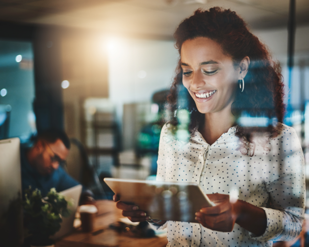Lächelnde Geschäftsfrau nutzt Tablet für digitales Arbeiten in einem modernen Open-Space-Büro