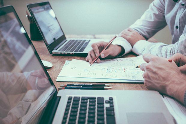 Zwei Personen bei der Arbeit mit Laptops und Unterlagen
