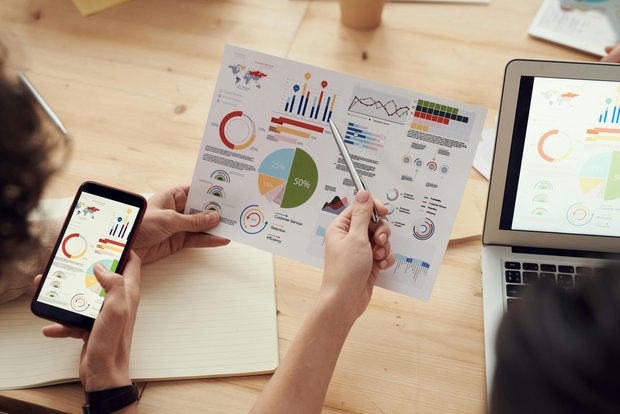 People analyzing data on paper, smartphone, and laptop