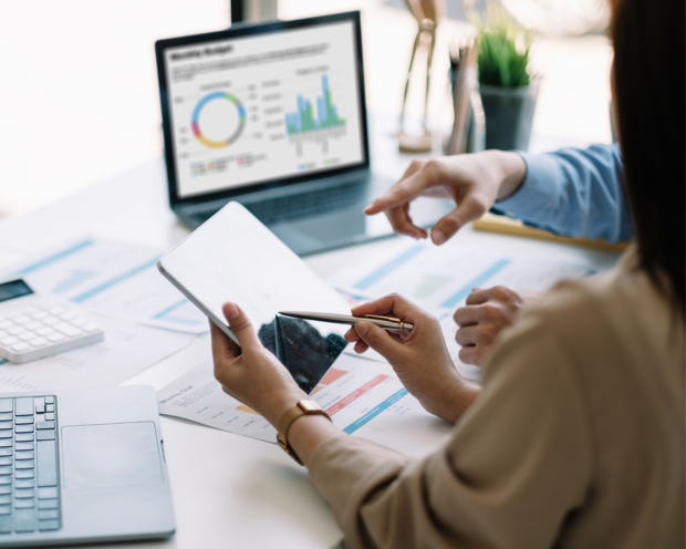Zwei Personen analysieren Geschäftsdaten mit Laptop, Tablet und Charts im Büro für strategische Entscheidungen